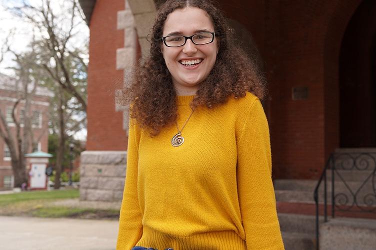 Woman student in a yellow sweater standing outside of Thompson Hall at UNH